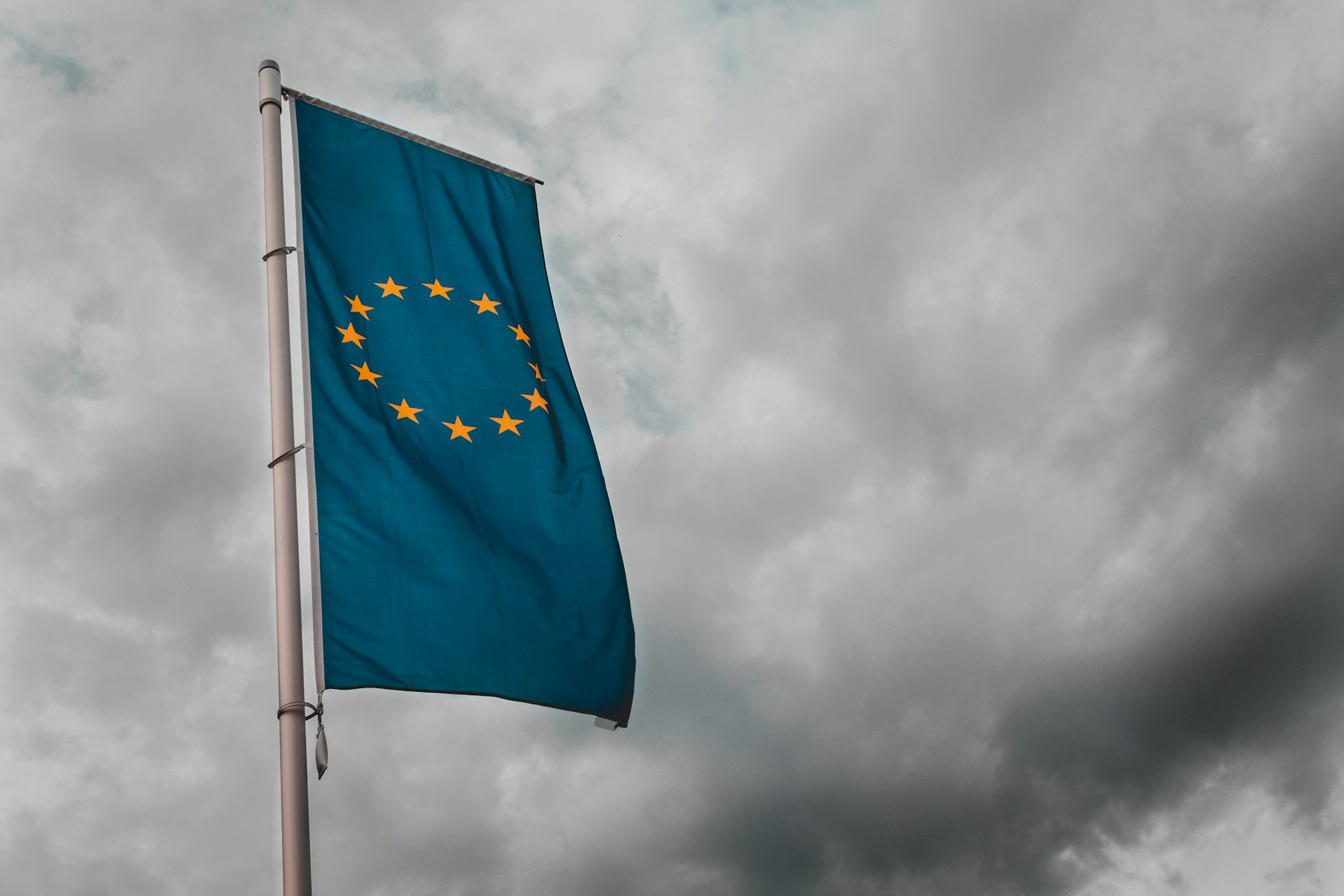 la bandiera dell'unione europea, stendardo gagliardo, si staglia contro lo scuro e temporalesco grigio cielo, forse di Brussele, Belgio