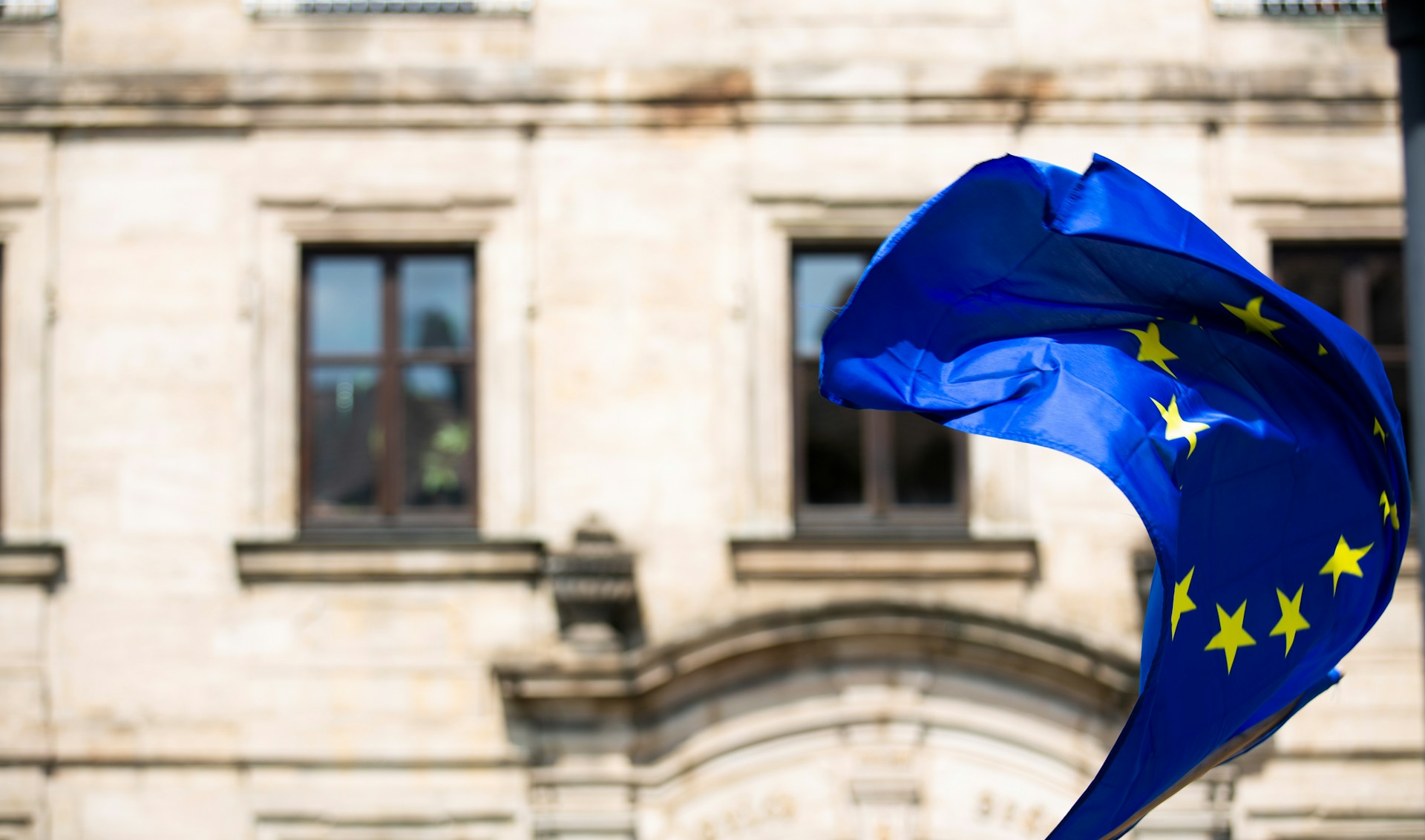 Una bandiera dell'Unione Europea garrisce fiera e gagliarda in questo periodo di avversità, di fronte a un marmoreo edificio bianco.