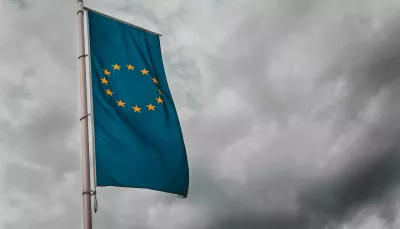 la bandiera dell'unione europea, stendardo gagliardo, si staglia contro lo scuro e temporalesco grigio cielo, forse di Brussele, Belgio