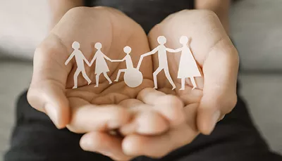 Mani che tengono sagome di carta di persone, una tra le quali portatrice di disabilità