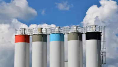 Cinque di quelle che sembrano taniche di stoccaggio industriali sono colorate verso la cima di grigio, azzurro e rosso, creando un piacevole effetto visivo