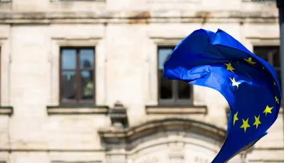 Una bandiera dell'Unione Europea garrisce fiera e gagliarda in questo periodo di avversità, di fronte a un marmoreo edificio bianco.