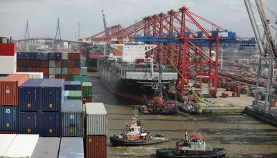 Due rimorchiatori operano nelle acque di un porto industriale. Sullo sfondo, mercantili, gru industriali e container. Si tratta proprio di supply chain.